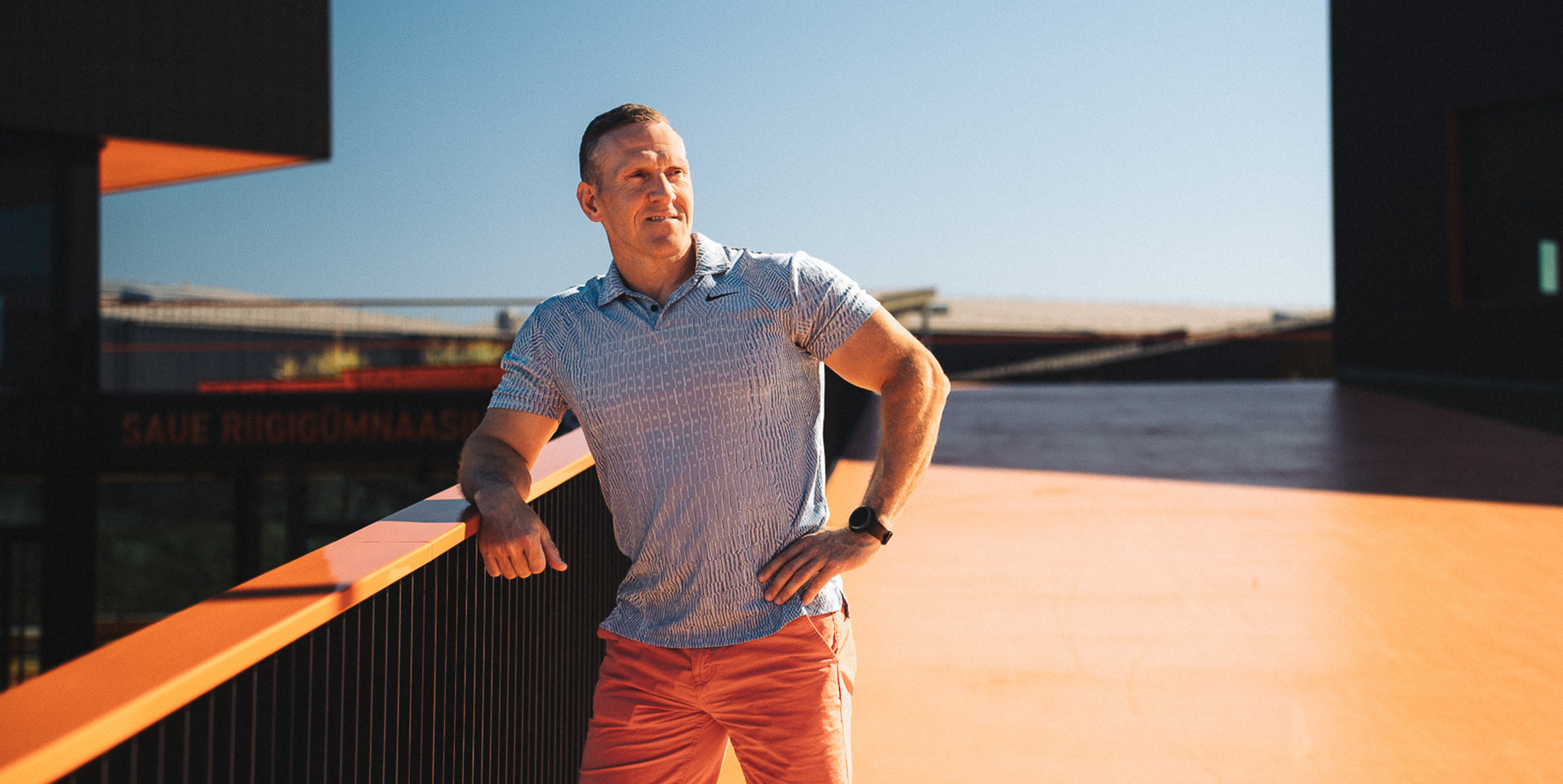 Mees seisab spordikompleksi rõdul päikesepaistelisel päeval, taustal Saue Riigiümnaasium