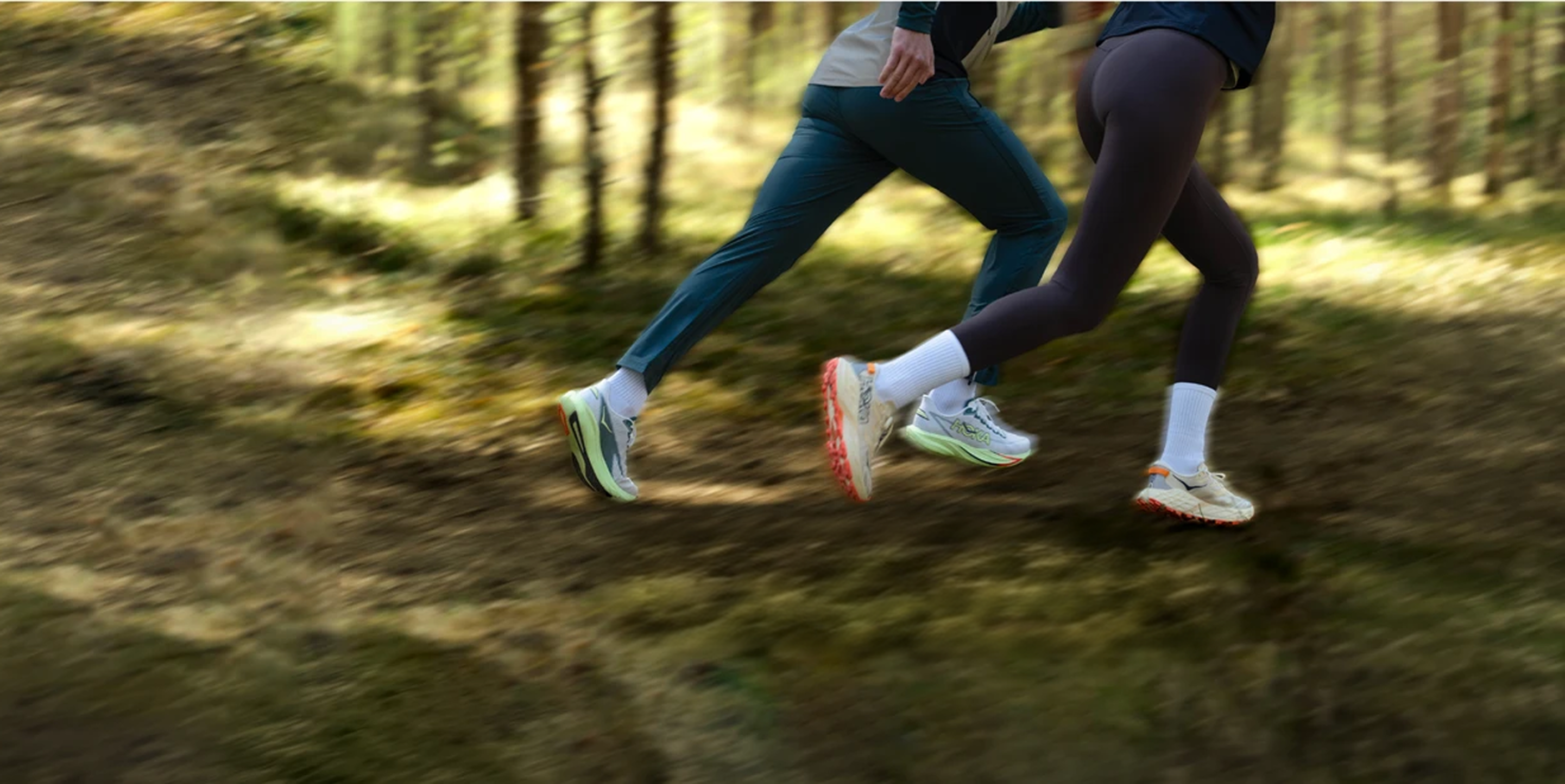 Kaks jooksjat liiguvad päikeselises männimetsas mööda metsarada, kaadris on jäädvustatud liikumishoog ja jalgade dünaamika.